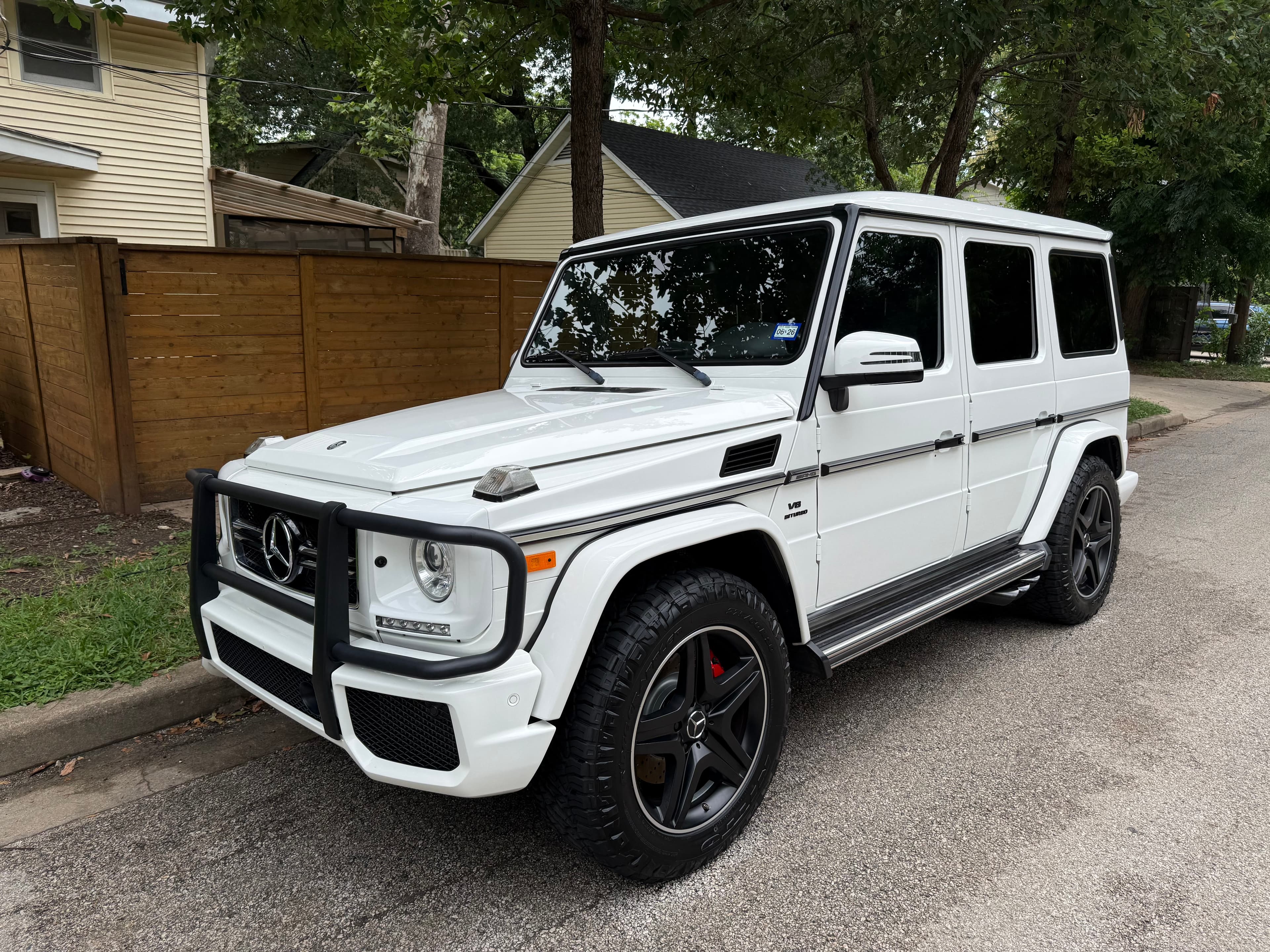 White Mercedes G-Class SUV with black wheels and brush guard parked on a street.
