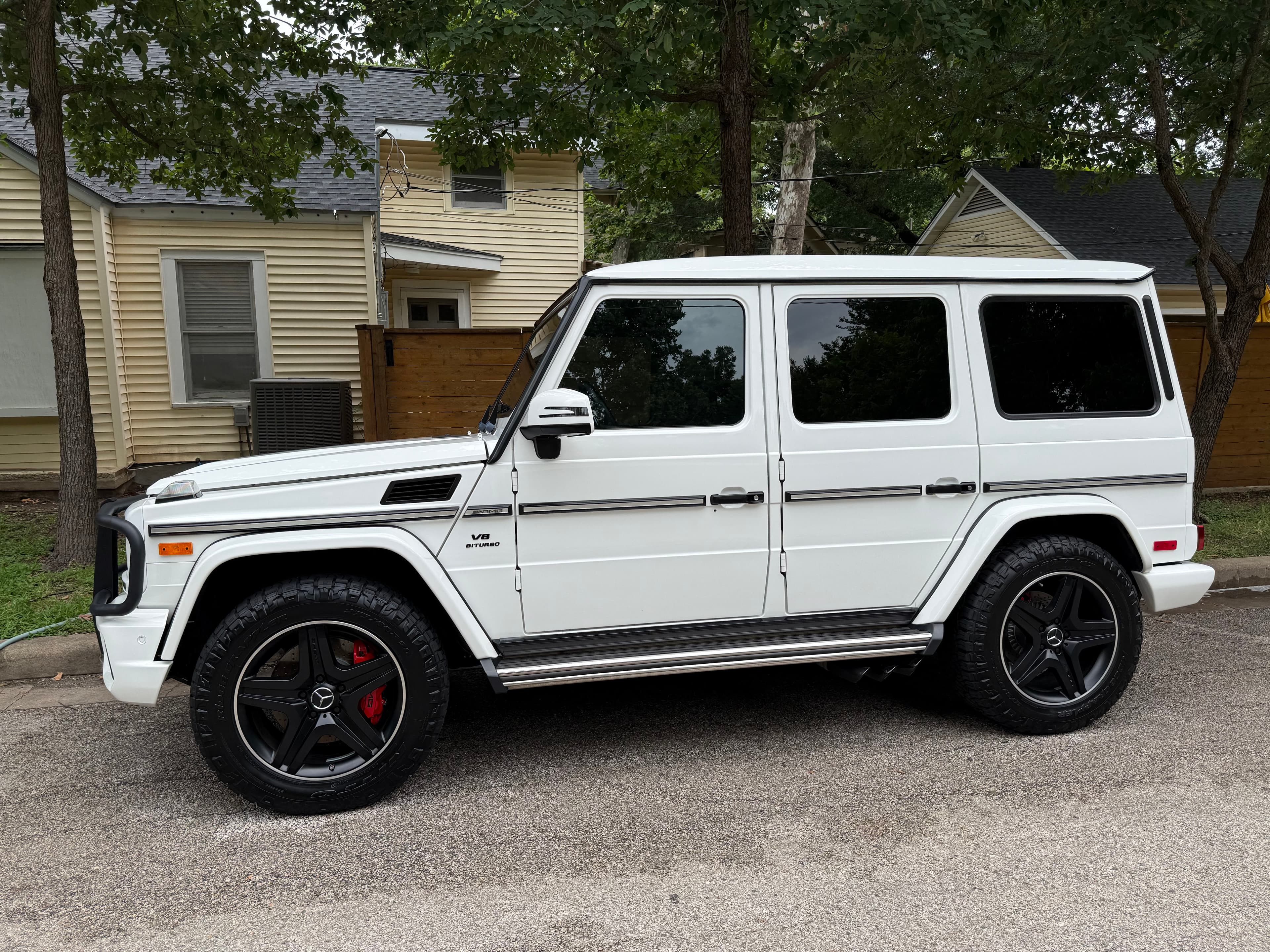 White Mercedes-Benz G-Wagon with black wheels and red calipers parked on a residential street.
