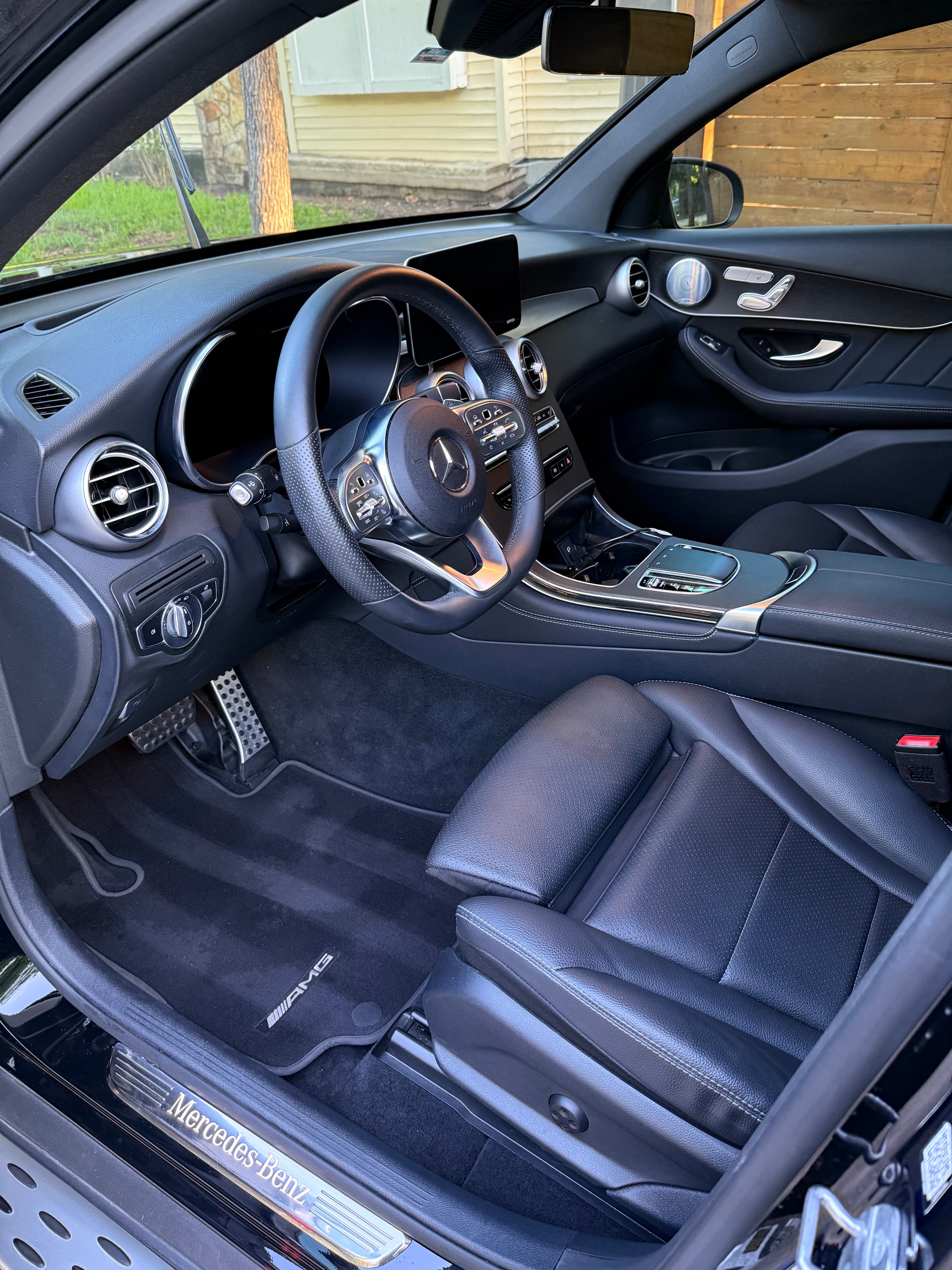 Black leather interior of a Mercedes-Benz featuring AMG floor mats and a multi-function steering wheel.