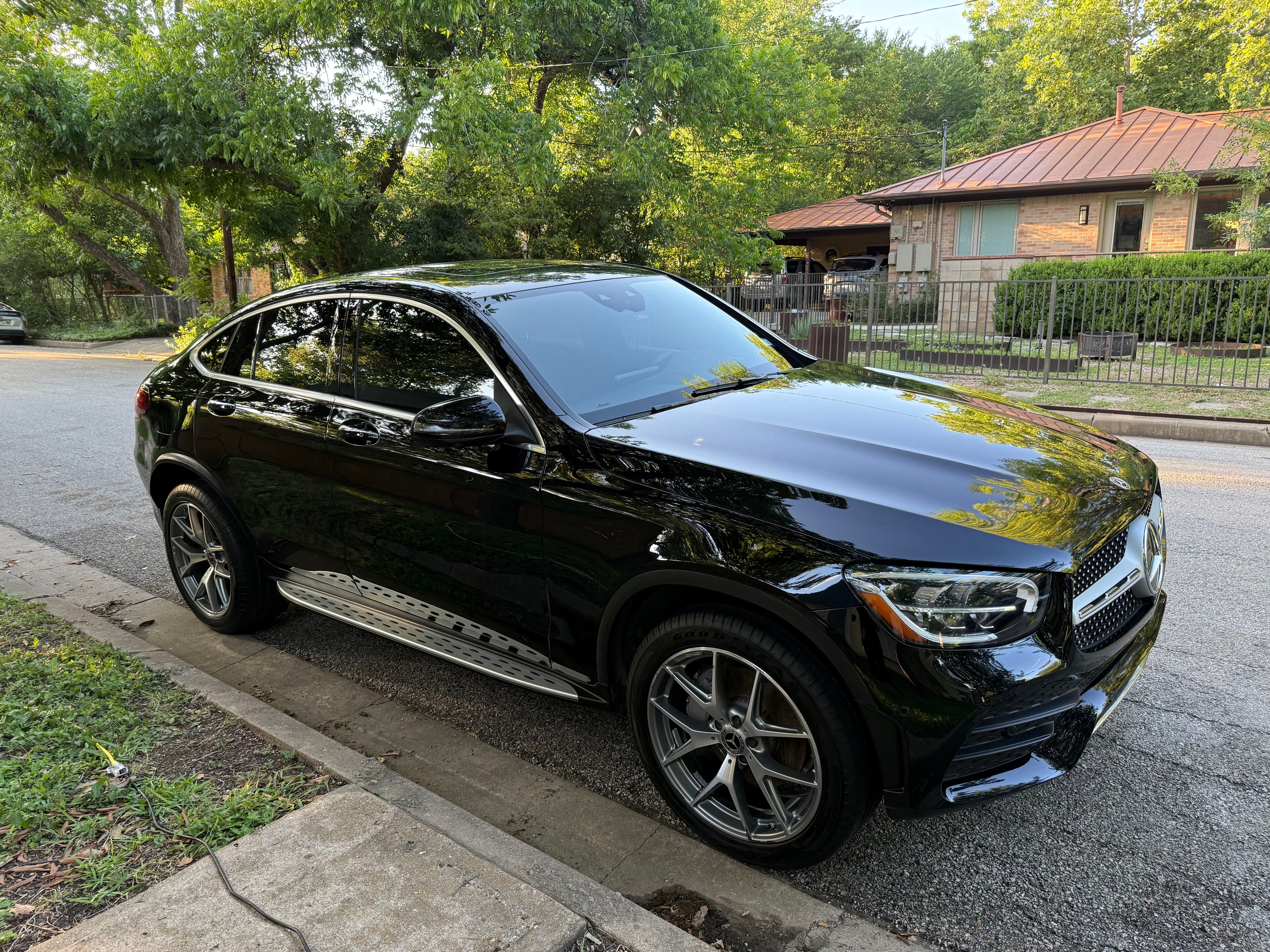 Glossy black Mercedes-Benz GLC Coupe parked on a residential street with lush green trees.