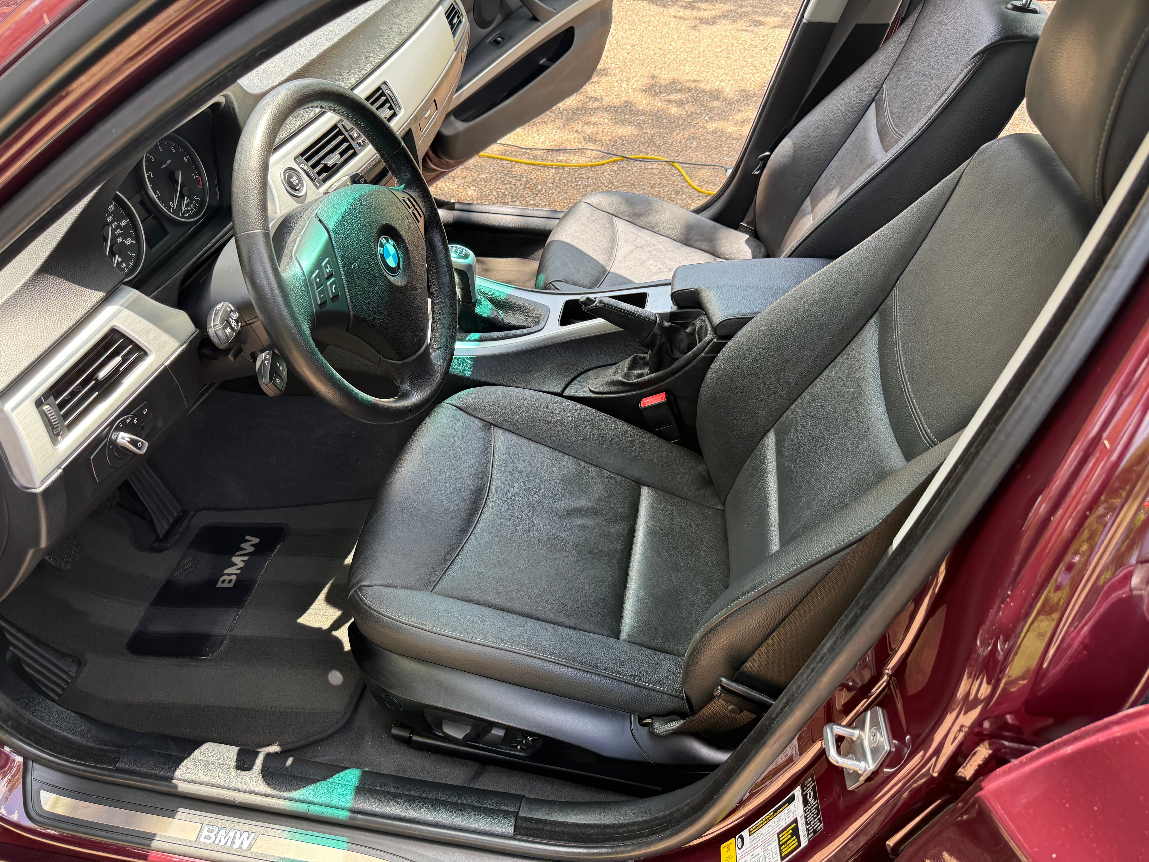 Interior of a maroon BMW with black leather seats, manual transmission, and steering wheel.